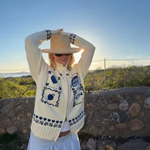 Model wearing cream knit cardigan with navy blue nautical patterns in an outdoor sunset scene