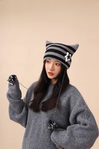 Model wearing a grey striped knit cat ear beanie with pompom strings and star patch