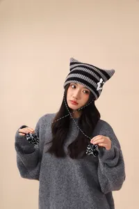 Close-up detail of cute cat ear striped knitted beanie with star patch and fuzzy pom-poms