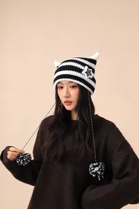 Detail of handmade striped cat ear beanie with star patch and pom-poms