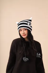 Close-up detail of a handmade black and white striped cat ear beanie with pom-poms.