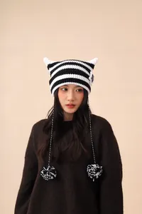 Close-up of a striped cat ear knit beanie with pom-poms worn by an Asian model