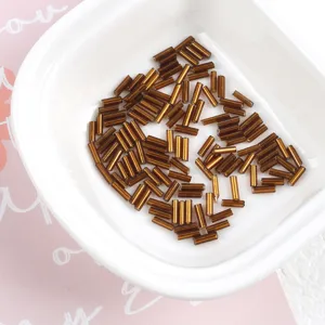 Close-up of 2x7mm metallic silver-lined brown glass bugle beads in a white dish.