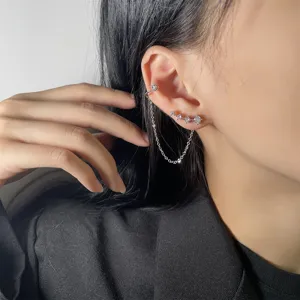 Primo piano di un ear cuff con zirconi brillanti con catena e orecchini a lobo argento.