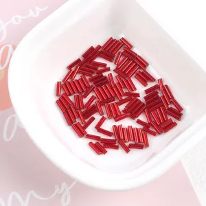Detailed view of red 2x7mm silver-lined glass bugle beads in a white bowl
