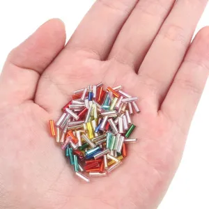 Mixed colorful 2x7mm silver-lined glass tube beads held in palm for DIY jewelry crafts