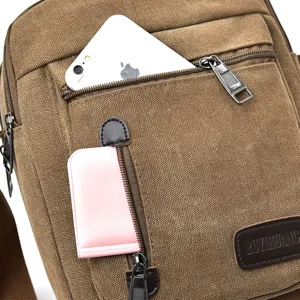 Brown canvas messenger bag with multiple compartments and a phone in the pocket.
