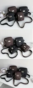 Display of black and dark brown men's oxford cloth small crossbody bags with straps.