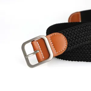 Close-up detail of black braided elastic belt with brown leather accent and silver pin buckle.