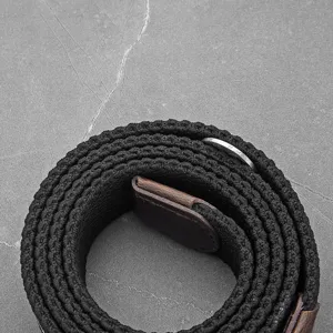Heren casual gevlochten elastische riem met bruine lederen uiteinden en metalen ring op steen.