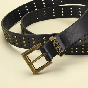 Detalle de cinturón ancho de cuero negro estilo punk con hebilla de metal y tachuelas.