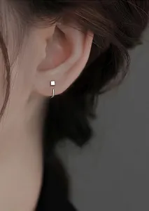 Close-up van minimalistische zilveren vierkante kubus oorbellen met geometrisch ontwerp.