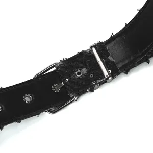 Close-up detail of punk style black distressed denim belt with metal grommets and buckle.