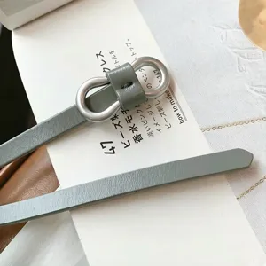 Detailed view of a slim sage green leather belt featuring a silver figure-8 metal buckle