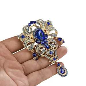 Élégante broche couronne dorée ornée de strass bleus et d'un pendentif goutte d'eau