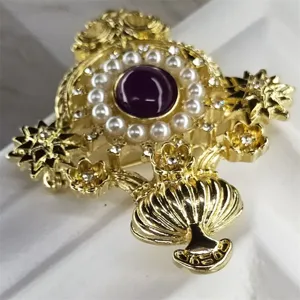 Dettaglio macro di una spilla barocca dorata con pietra viola e perle eleganti