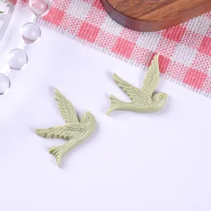 Close-up view of two light green resin swallow bird charms for DIY creative jewelry