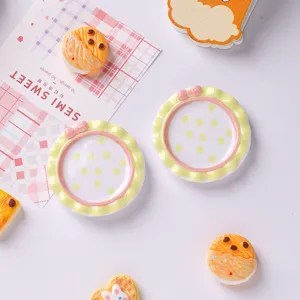 Gros plan d'assiettes miniatures en résine avec bords ondulés jaunes et nœuds roses