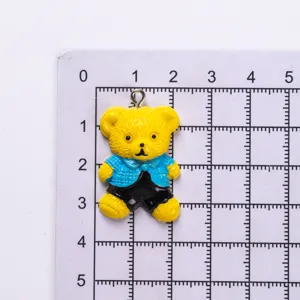 Detail view of a small yellow resin teddy bear charm shown on a measuring grid for scale.