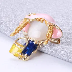 Close-up detail of a cute cartoon girl brooch with pink hat and cat-eye stone face decoration.