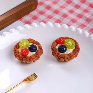 Nahaufnahme von realistischen Miniatur-Obsttörtchen mit Erdbeer-, Kiwi- und Blaubeerbelag.