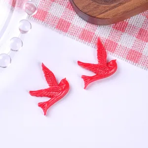 Close-up detail of two red resin swallow bird charms for DIY jewelry and hair accessories