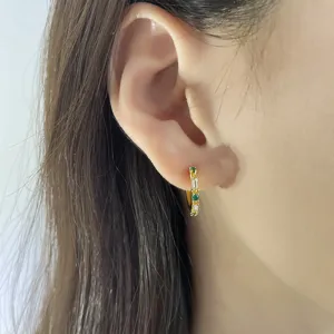 Vista detallada de elegantes aros dorados con circonitas verdes y blancas puestos en la oreja