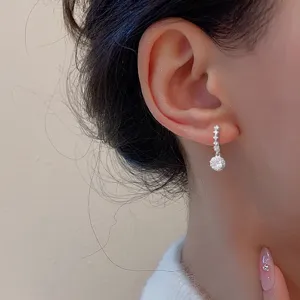 Gros plan de boucles d'oreilles pendantes en zircon rond étincelant sur une oreille.