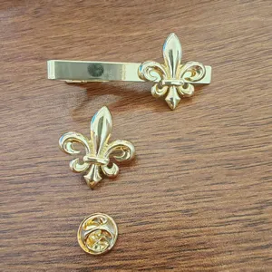 Detail view of a gold fleur-de-lis tie clip and matching lapel pin set for men.
