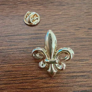 Detailed shot of a vintage gold fleur-de-lis lapel pin with butterfly clutch on wood