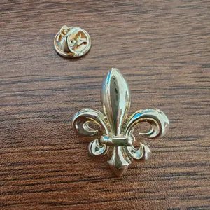 Macro view of a classic gold-toned fleur-de-lis lapel pin on a wooden surface.