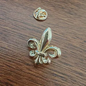 Detailed close-up view of a golden fleur-de-lis lapel pin and its clutch back on wood