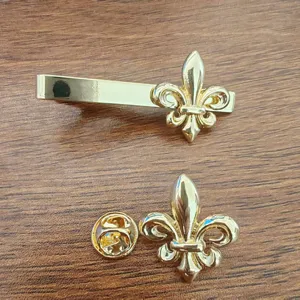Close-up detail of the elegant gold Fleur-de-lis patterned tie clip and lapel pin set.