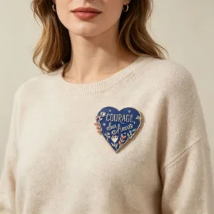 Detailansicht einer blauen Emaille-Herzbrosche mit dem Text 'Courage, dear hearts'.