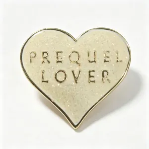 Macro detail of a vintage heart-shaped glitter enamel pin with PREQUEL LOVER gold lettering