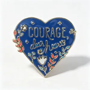 Detailansicht der blauen Herzbrosche aus Emaille mit Schriftzug 'Courage, dear heart'.