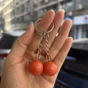Detailopname van een 2 cm oranje cricketbal-stijl dubbele sleutelhanger in de hand gehouden