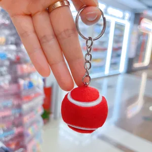Detalle de un llavero de pelota de tenis roja suave sostenido por una mano en una tienda