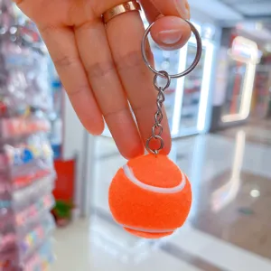 Detalle de un llavero de pelota de tenis naranja con anillo y cadena de metal plateado.