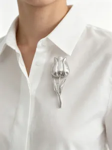 Primo piano di un'elegante spilla a tulipano argento appuntata su una camicia bianca.