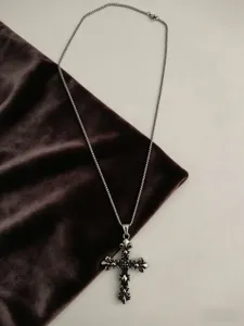 Close-up detail of vintage fleur-de-lis cross pendant on a textured velvet backdrop