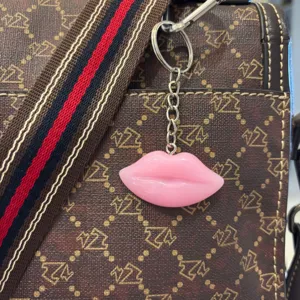 Detail shot of a glossy pink resin lip keychain hanging on a stylish brown patterned bag