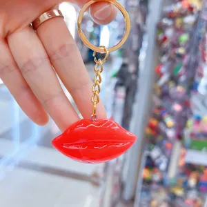 Glossy red resin lip keychain charm held by hand in a detail view