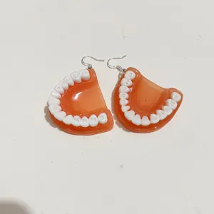 Quirky handmade resin denture earrings with realistic white teeth detail on flesh-tone base.