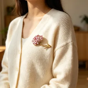Detail of an enamel carnation flower brooch worn on a cream-colored cardigan