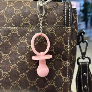 Detail eines rosa Schnuller-Schlüsselanhängers an einer braun gemusterten Tasche