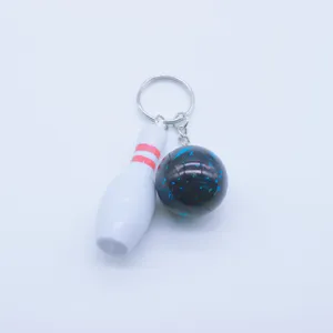 Close-up detail of a mini white bowling pin and black ball keychain with blue accents