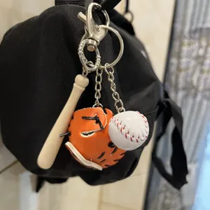 Miniature baseball bat glove and ball keychain hanging on a black backpack detail view