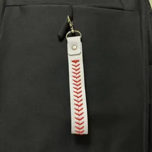 Detail showing a white baseball stitch bag charm with red embroidery on a black bag.