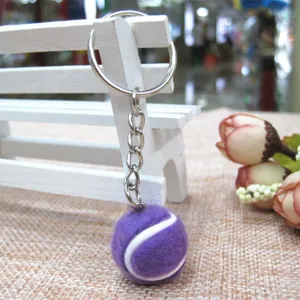 Detailweergave van een paarse mini tennisbal sleutelhanger met metalen ring en ketting op bank